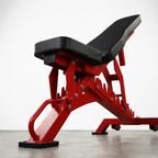 Adjustable weight bench with a red metal frame and black padded seat and backrest, photographed on a light gray studio background.