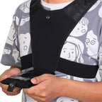 Person wearing a black vest with straps, holding a device.