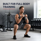 A man in a gym performing a deep squat while holding a black kettlebell. He is wearing a dark gray tank top, shorts, and black athletic shoes.