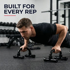 A man in a black shirt performs pushups using black underbarrel pushup stands in a gym setting, with the text 'BUILT FOR EVERY REP' in the top left corner.