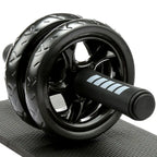 A black double-wheel ab roller with ergonomic handles and a high-density knee pad, placed on a textured surface.