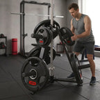A man in a gym setting using a black and silver weight rack with loaded 20kg weight plates. The man is wearing a gray tank top and dark gray shorts.