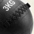 Close-up of a black heavy medicine ball with white '3KG' text and black stitched laces, shown against a light neutral background.