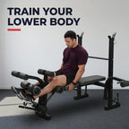 A man sits on a black leg extension gym machine in a minimalist gray room, wearing a dark maroon t-shirt and black shorts. The text 'TRAIN YOUR LOWER BODY' is displayed in the upper left corner.