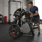 A man in a gym setting loads a 20kg weight plate onto a black and silver weight rack stand. The rack is loaded with several black weight plates, some featuring red '20KG' labels.
