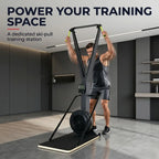 A man using a large black ski-pull training machine in a modern gym interior. The machine has a rectangular base, a large circular flywheel, and a tall angled pull-up frame with yellow handles.