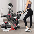 Woman using a stationary bike in a home setting with a focus on the bike's wheel.