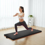 Woman performing a yoga pose on a black exercise mat in a bright room.