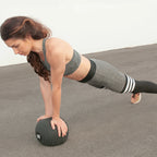 Woman in athletic wear performing a push-up with a medicine ball on a plain background