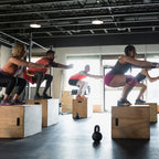 Group of people performing box jumps in a gym.