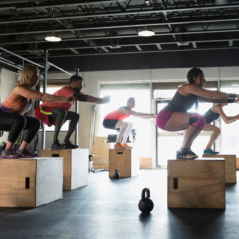 Group of people performing box jumps in a gym.