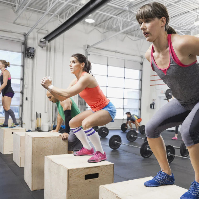 Group of people performing box jumps in a gym.