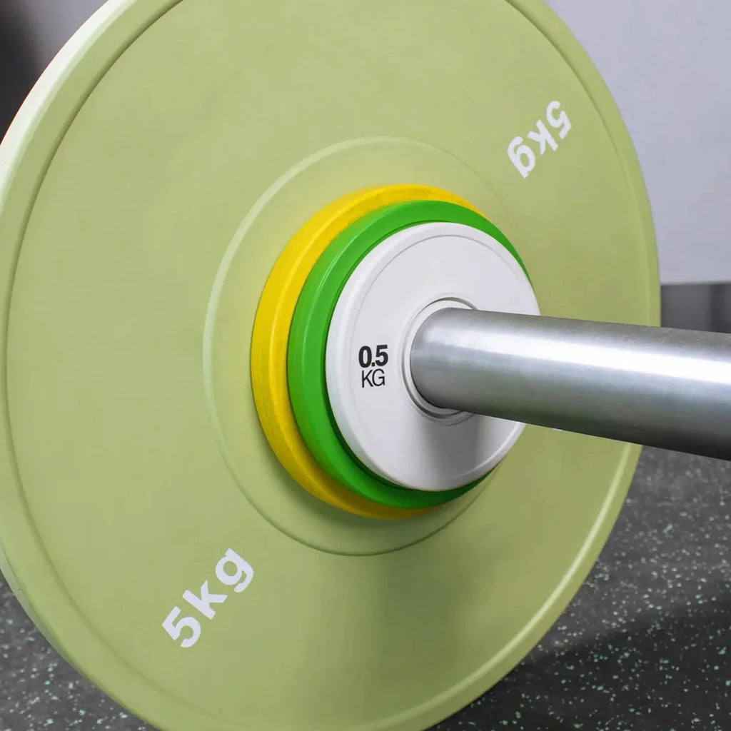 Close-up of a barbell with green weight plates on a gray surface
