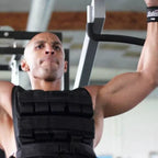 Man performing pull-ups in a gym wearing a black weight vest.